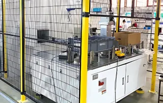 Safety fence industrial cell enclosing a white automation machine with black mesh and yellow posts
