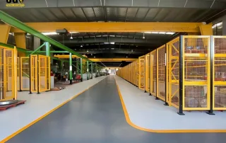Cercas de segurança para máquinas com mudanças frequentes de layout — visão ampla da cerca de segurança industrial modular Mdfence amarela ao longo de um corredor de armazém