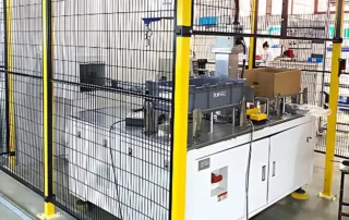 Vista principal da proteção de perímetro industrial com tela preta da cerca de segurança robótica Mdfence envolvendo uma máquina de automação branca