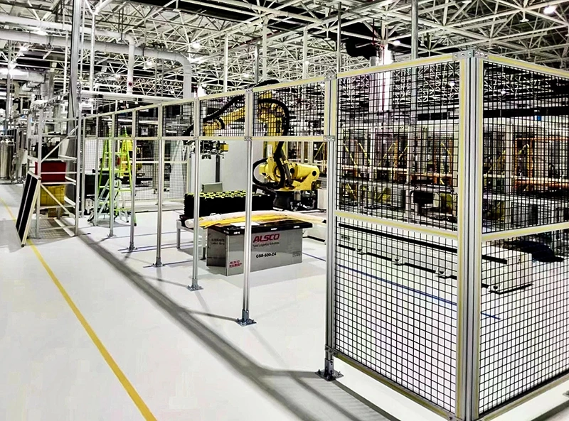 Industrial safety fence enclosure with welded mesh panels, anchored posts, and yellow robotic arms