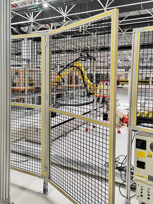 Equipment isolation fence with welded wire mesh panels, hinged access doors, and floor anchors for automated equipment isolation