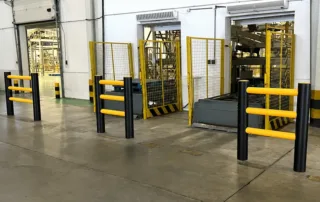 Factory-installed steel safety barrier posts with yellow rails and mesh gates around conveyor openings