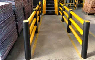 Factory-installed yellow dual-rail safety barrier with black bollards for pedestrian and equipment segregation.