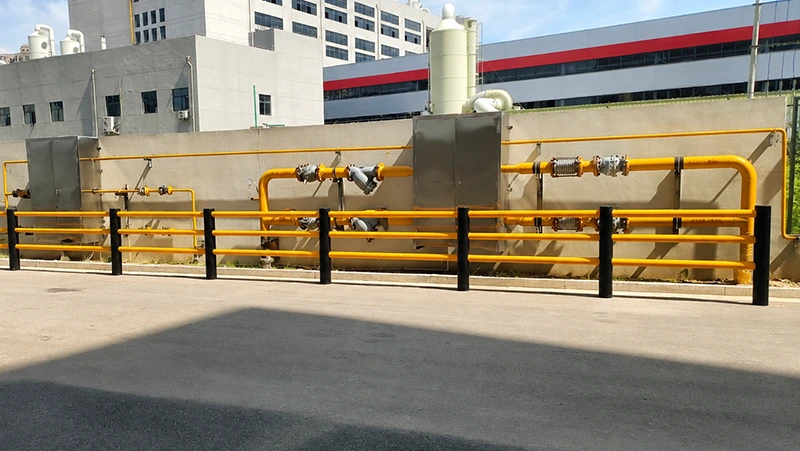 Outdoor yellow steel pipeline barrier with flanged joints, expansion joint, and protective rail posts