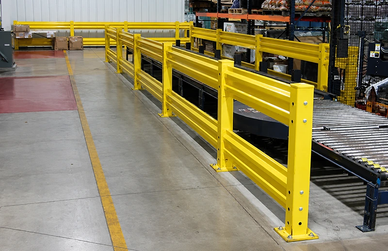Yellow heavy-duty steel guard rails with double corrugated rails protecting an industrial roller conveyor