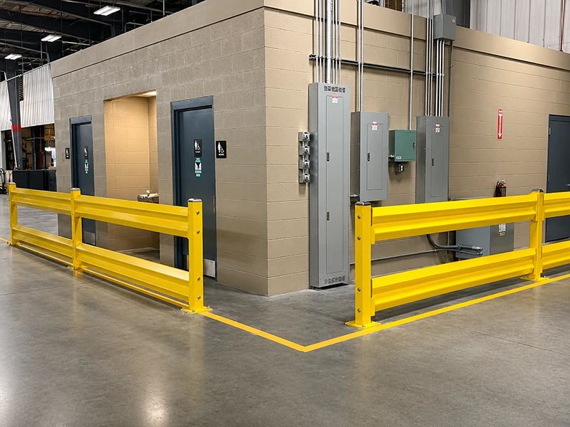 Yellow dual-rail steel forklift barrier protecting warehouse electrical rooms with anchored square posts and corrugated panels