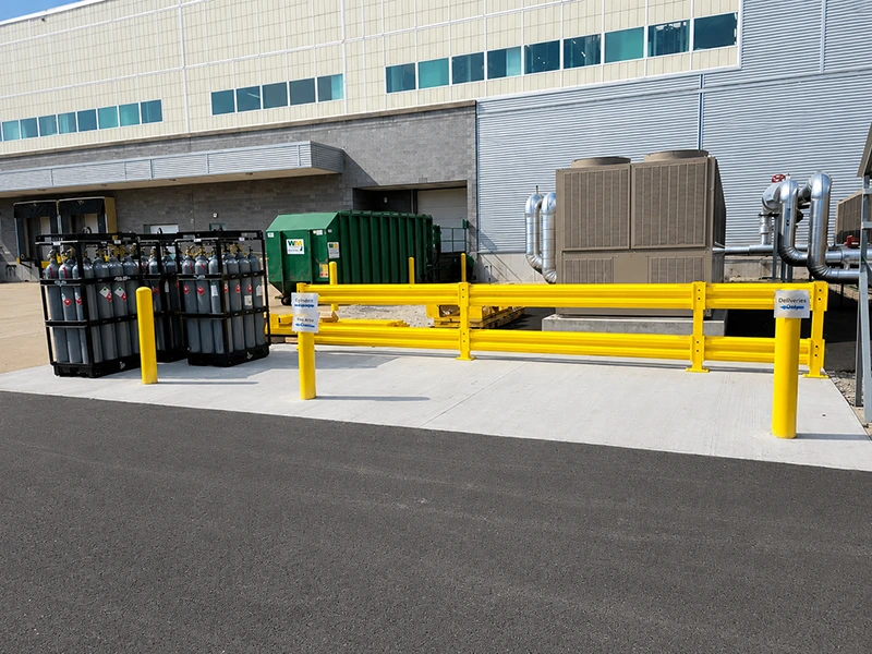 Yellow double-rail corrugated safety barrier with bollards protecting industrial equipment from forklift impact
