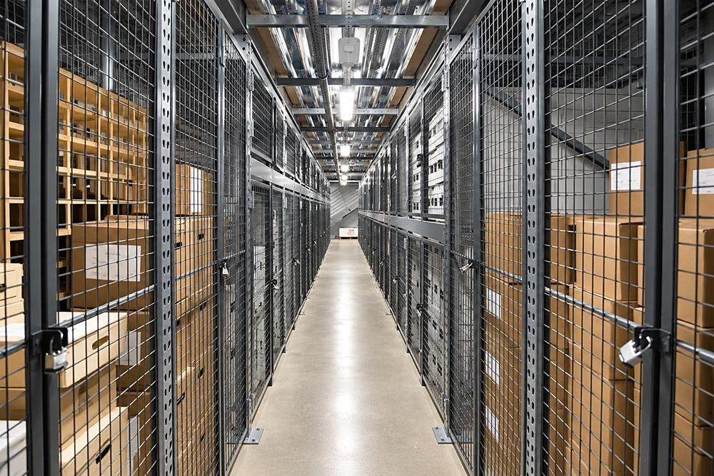 SGF stlk metal wire mesh partition cages in warehouse aisle featuring lockable doors and internal wooden shelving for secure storage.