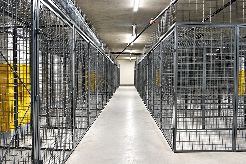 Industrial wire mesh partition cages forming a secure warehouse aisle with lockable grid doors and steel frames.